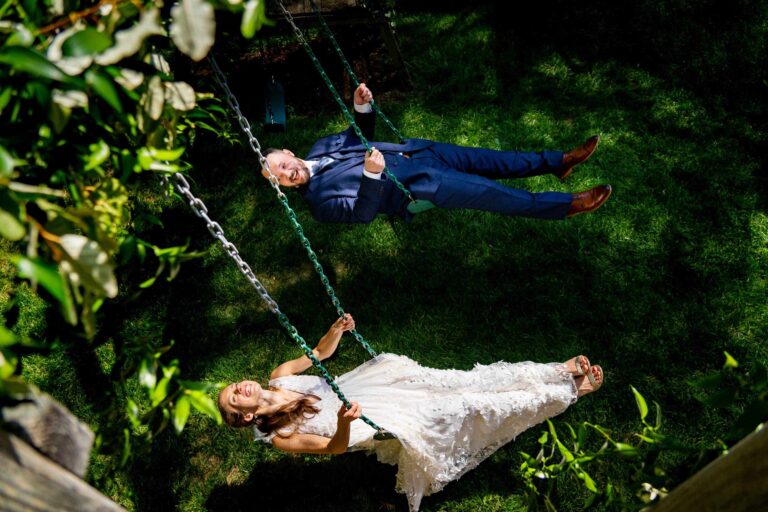 A bride and groom laugh as they swing on a children's playset during their wedding