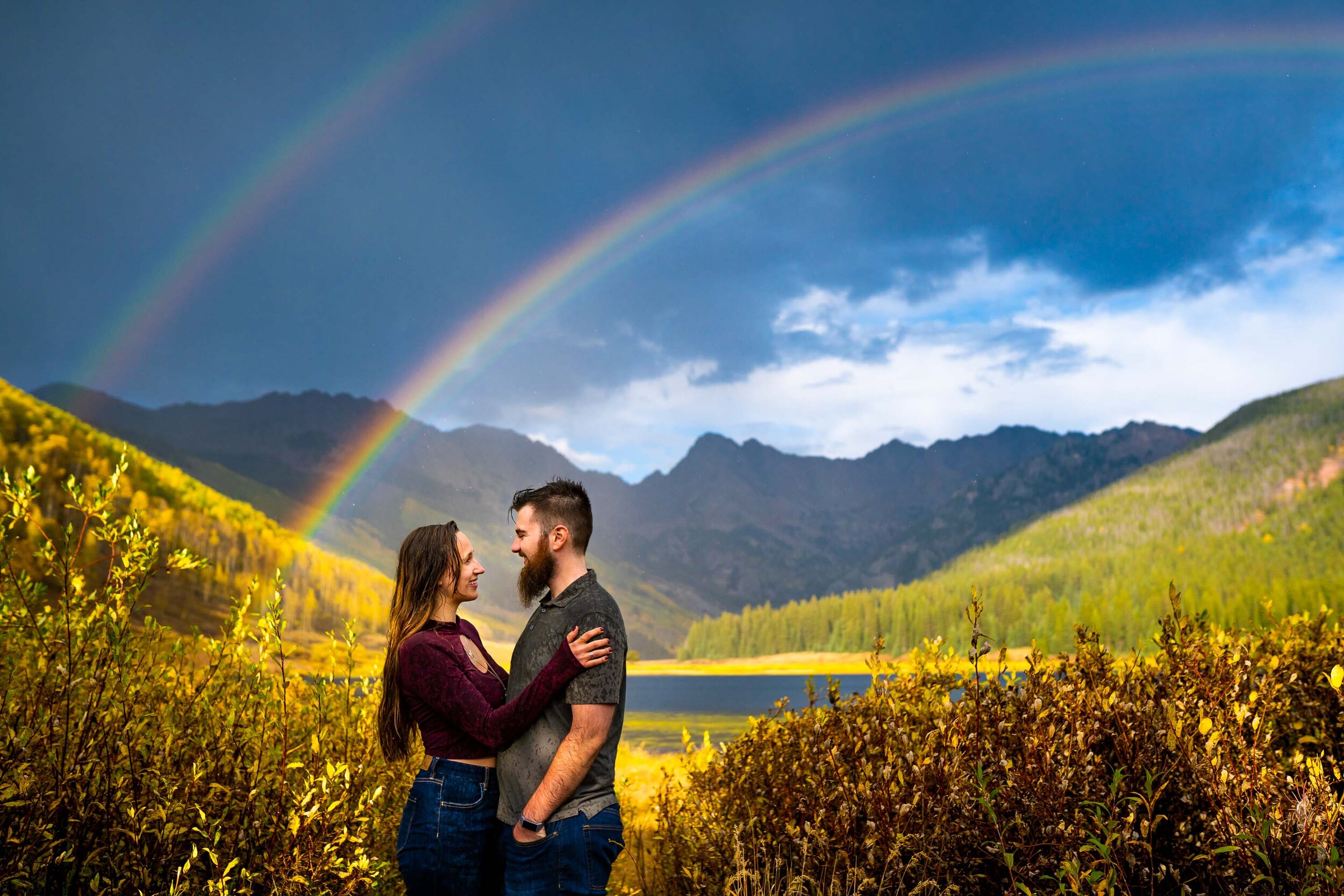 Engaged couple embraces for a portrait during a rainstorm with a double rainbow behind them arching over Piney Lake, Engagement Session, Engagement Photos, Engagement Photos Inspiration, Engagement Photography, Engagement Photographer, Fall Engagement Photos, Mountain Engagement Photos, Piney River Ranch engagement photos, Vail engagement session, Vail engagement photos, Vail engagement photography, Vail engagement photographer, Vail engagement inspiration, Colorado engagement session, Colorado engagement photos, Colorado engagement photography, Colorado engagement photographer, Colorado engagement inspiration