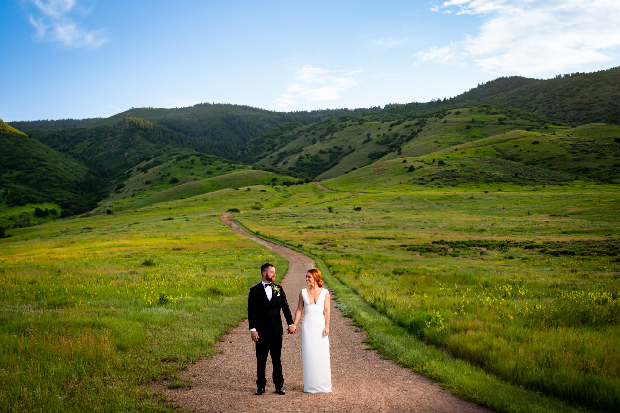 A bride and groom stand holding hands during portraits at their summer Manor House wedding in Littleton, Colorado