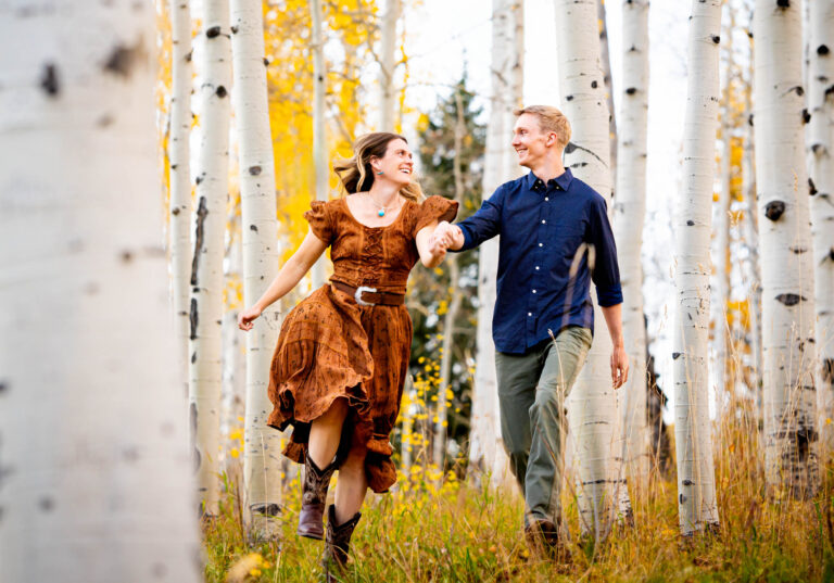 Documentary style engagement photos of an engaged couple holding hands and running through a golden aspen grove in the mountains in the fall at Kebler Pass in Created Butte.