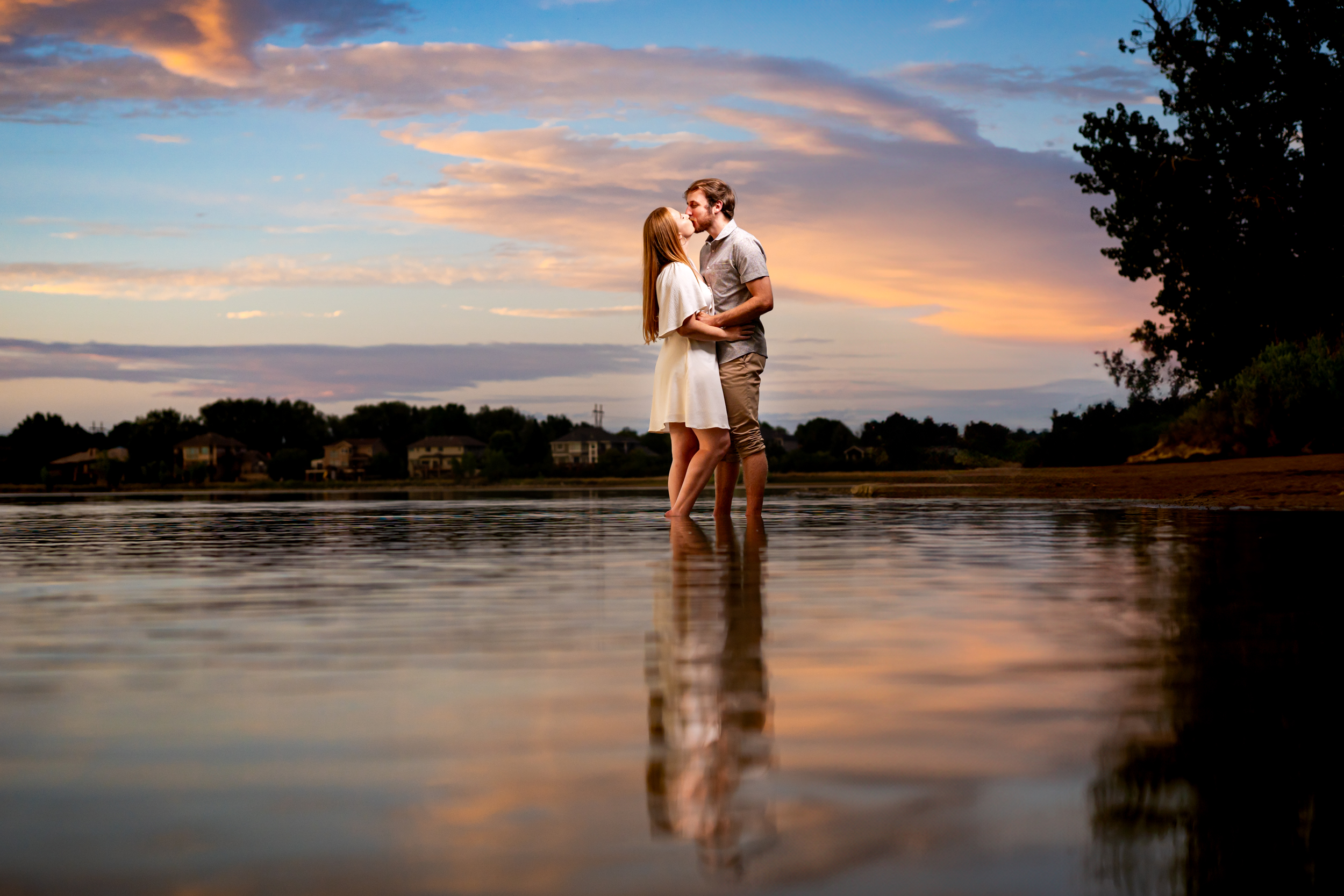 Newly engaged couple kisses in the water at sunset at McIntosh Lake in Longmont