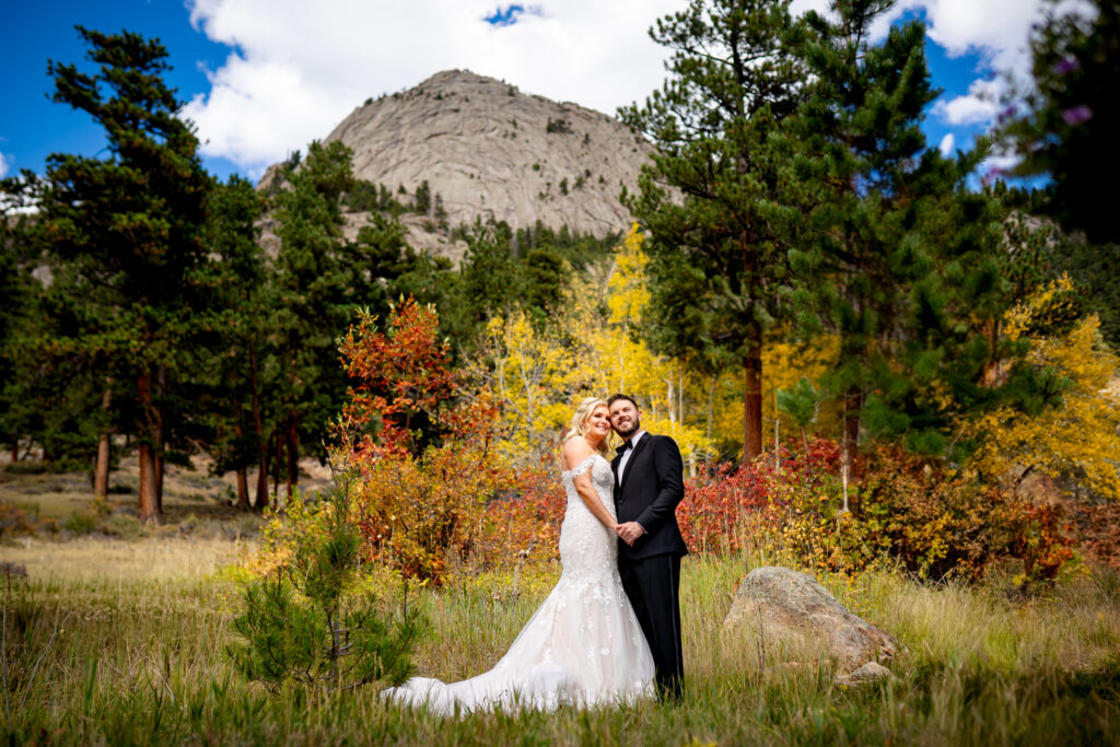 A bride and groom stand in front of golden aspens and McGregor Mountain during their Della Terra Mountain Chateau wedding