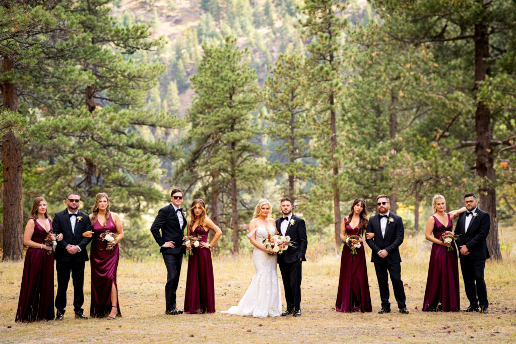 A stylish wedding party poses for photos in a grassy meadow surrounded by pine trees during a Della Terra Mountain Chateau wedding