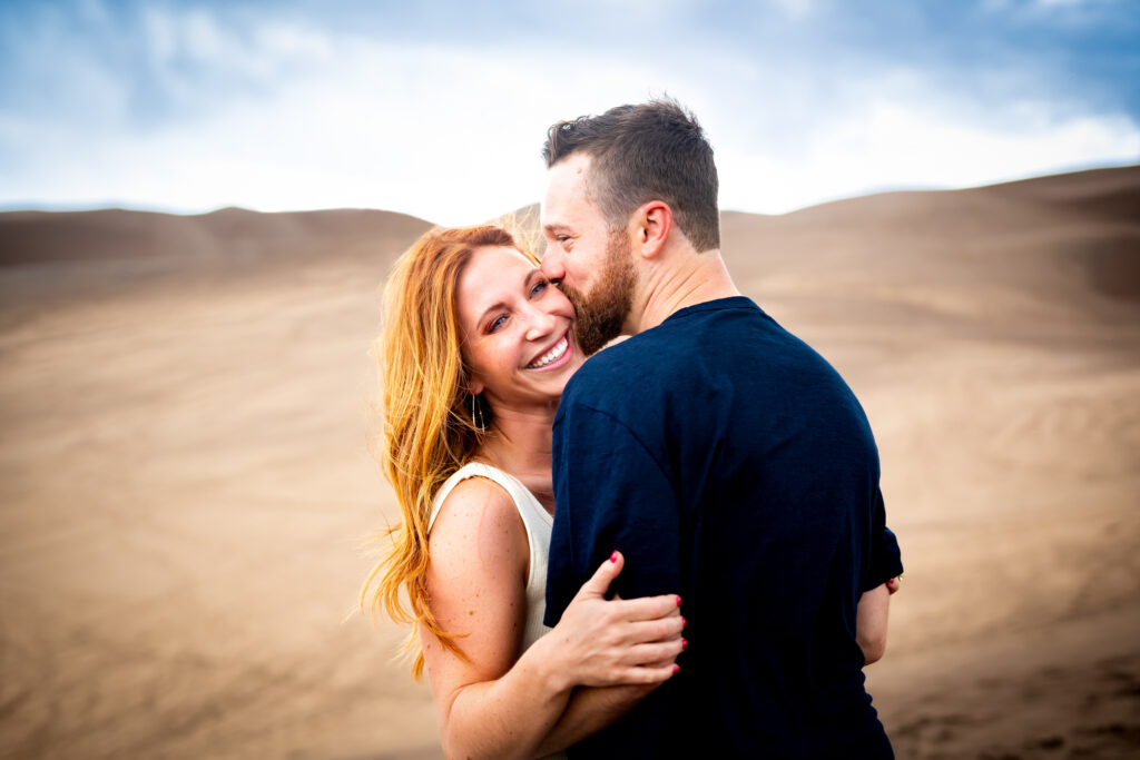 A couple embraces with the Great Sand Dunes behind them