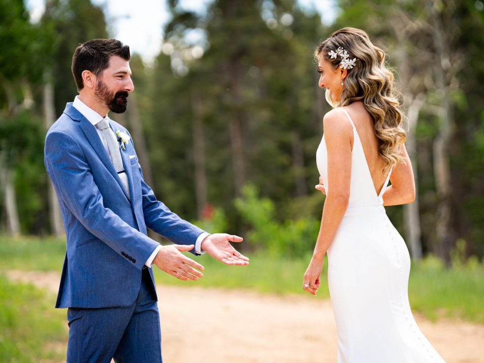 A groom stands with his arms out in surprise at how beautiful his bride is during their first look at Dao House