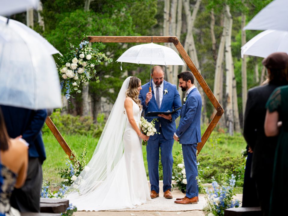 A bride and groom stand at the Dao House ceremony site under umbrellas