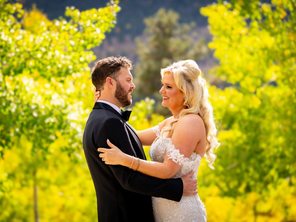 A bride and groom smile while embracing in front of golden aspens during their fall Della Terra Mountain Chateau wedding