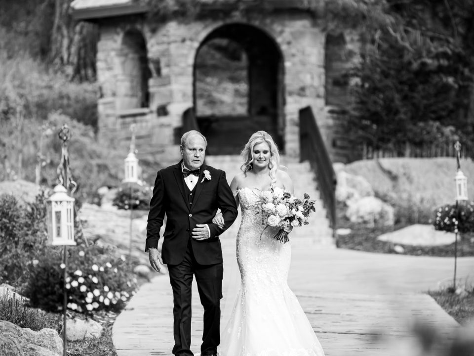 A bride's father walks her down the aisle before her wedding ceremony at Della Terra Mountain Chateau